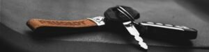 High contrast, artistic shot of a car key on a black surface with a leather keychain.